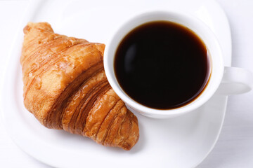 Tasty breakfast. Cup of coffee and croissant on white wooden table, above view