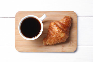 Tasty breakfast. Cup of coffee and croissant on white wooden table, top view