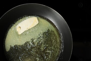 Melting butter in frying pan on cooktop, top view