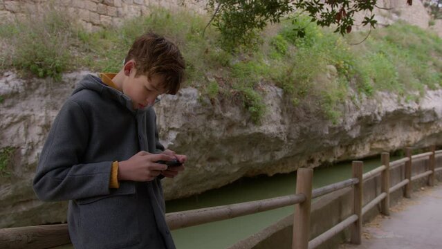 The teenager is focused on his mobile phone, and behind him you can see the mountain and the river
