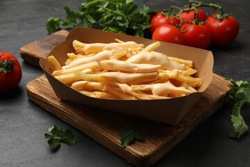 Tasty potato fries, cheese sauce in paper container and products on black table, closeup