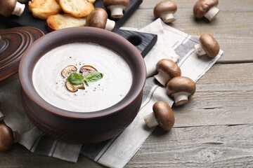 Delicious homemade mushroom soup in ceramic pot and fresh ingredients on wooden table. Space for...