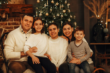 Mother, father and children decorate the tree in room. Loving family indoors