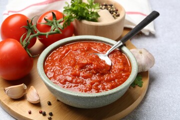 Homemade tomato sauce in bowl, spoon and fresh ingredients on light grey table