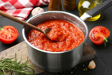 Homemade tomato sauce in pot, spoon and fresh ingredients on dark table