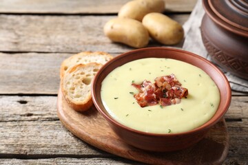 Tasty potato soup with bacon in bowl and cut bread on wooden table