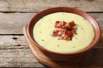 Tasty potato soup with bacon and rosemary in bowl on wooden table, closeup