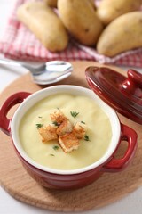 Tasty potato soup with croutons and rosemary in ceramic pot on white table, closeup