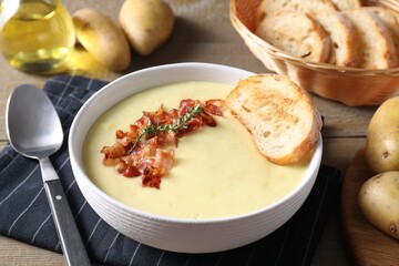 Tasty potato soup with bacon and rosemary in bowl served on wooden table