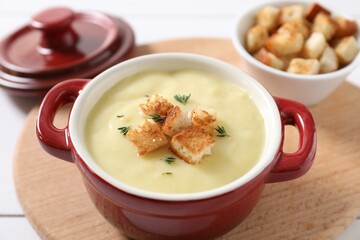 Tasty potato soup with croutons and rosemary in ceramic pot on white table, closeup