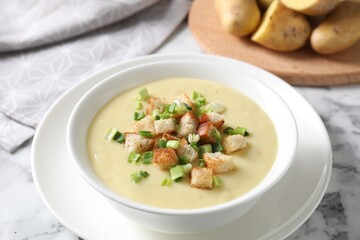 Tasty potato soup with croutons and green onion in bowl on white marble table