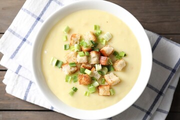 Tasty potato soup with croutons and green onion in bowl on wooden table, top view