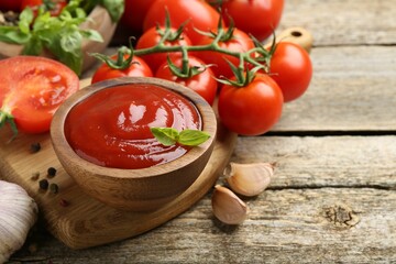 Tasty ketchup, fresh tomatoes, basil and spices on wooden table. Space for text