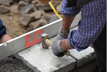 close up mani muratore al lavoro con martello costruzione muro di pietra sassi 