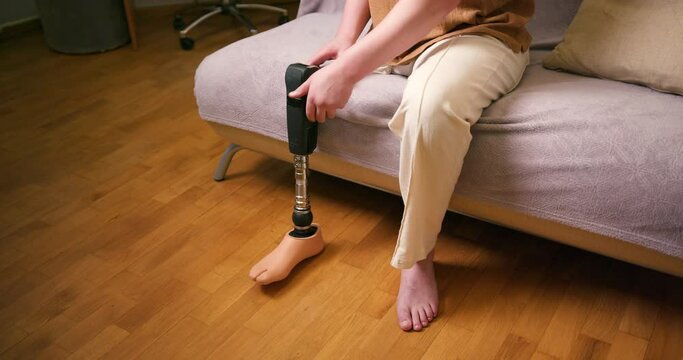 Close up of man amputee with prosthetic leg disability on above knee transfemoral leg prosthesis artificial device sitting at home. People with amputation disabilities everyday life