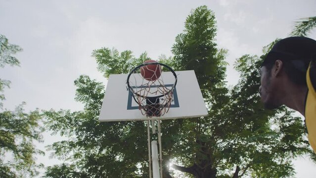 Low angle view of male athlete of African American ethnicity shooting ball in streetball ring outdoors