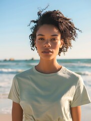 Woman wearing light sage t-shirt for a mockup design, in background beach