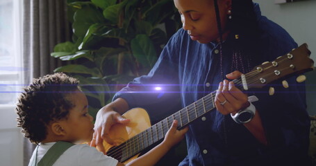 In this image, a young black mother and her son are playing the guitar together in their living room