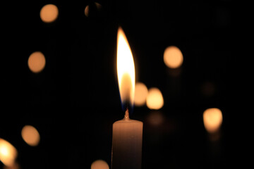Close-up of the flame of candle in the dark in church with bokeh background. Candle light with copy space.