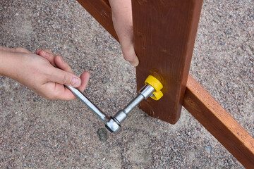 Tightening mounting bolt with ratchet socket wrench when assembling outdoor furniture. - obrazy, fototapety, plakaty