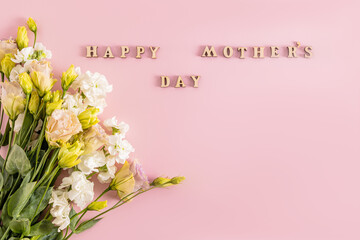 Beautiful bouquet in light colors of spring flowers on pink background with wooden letters and mother's day wish text. Holiday concept.