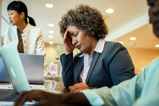 Stressed businesswoman with headache working at office desk with colleagues