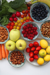 Apples, lemons, bananas, berries, carrots, leek, tomatoes, radishes, spinach and various nuts on white background. Healthy seasonal fruit and vegetable. Top view.