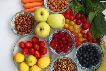 Apples, lemons, bananas, berries, carrots, leek, tomatoes, radishes, spinach and various nuts on white background. Healthy seasonal fruit and vegetable. Top view.