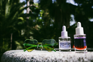 Tropical summer cosmetics. Cosmetic serum, oil extracts against lush greenery of tropics. Skin care products. Beauty nature. Heart-shaped sunglasses.