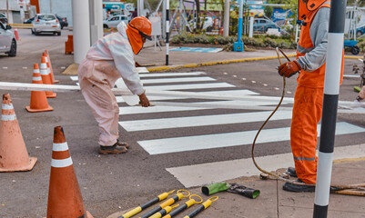 Three men in orange work clothes are painting a crosswalk