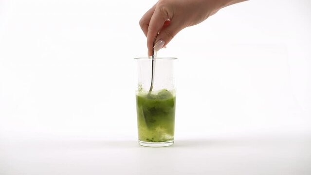 Transparent glass with green powder being mixed by a fork, creating bubbles in a white setting