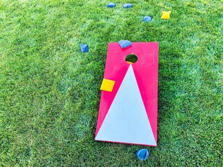 Red and white cornhole board with bean bags on lawn in summer, leisure game activity