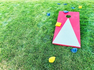 Red and white cornhole board with bean bags on lawn in summer, leisure game activity © valbunny