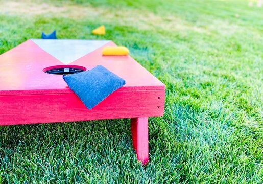Red and white cornhole board with bean bags on lawn in summer, leisure game activity