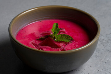 Cold beetroot soup with mint in a bowl on a gray background