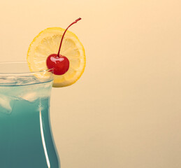 Classic blue lagoon cocktail garnished with lemon slice and cherry on warm beige background with...
