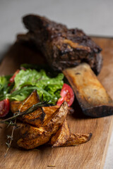 roasted veal rib with baked potatoes and vegetables on a wooden board