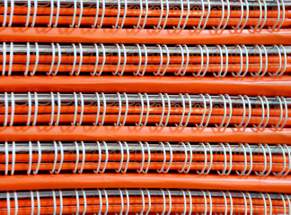 background of stack of orange notebooks with white spiral wire ties. coiled wire in book binding