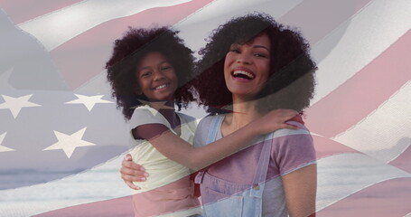 Composite image of american flag over african american mother and daughter smiling at the beach - obrazy, fototapety, plakaty