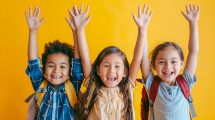 Three Joyful multiracial Schoolchildren With Backpacks Raising Hands High Celebrating back to school Against a Yellow Background