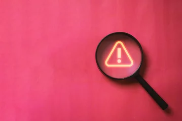 Poster Glowing red triangle caution warning or exclamation sign inside magnifier glass for notification error and maintenance concept. © Dilok