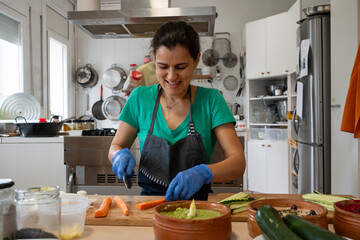Woman sitting in a kitchen cutting carrots, smiling. Cook in her forties with smiling apron and...