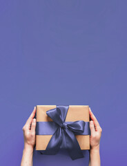 Female hands hold gift box on violet 2020 color