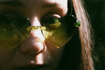 Young happy woman wearing green heart shaped sunglasses closeup portrait. White smiling millennial girl in summertime. Cheerful lady looking in camera