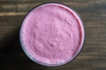 Raspberry banana smoothie in glass on a wooden table, closeup, top view - 785509402
