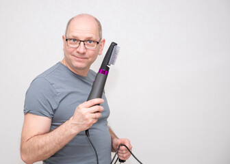 Bald Caucasian man 50 years old wearing glasses, smiling and using an electric hair comb