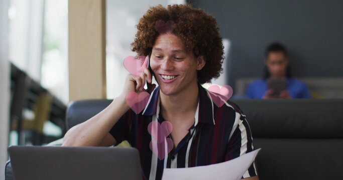 Image of red hearts over biracial businessman using smartphone