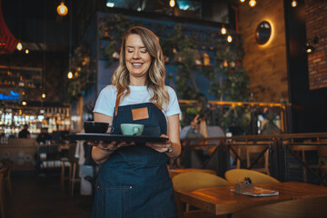 Portrait of a happy waitress working at a restaurant and looking at the camera smiling. I Love My Job! Waitress is laughing and enjoying being at work, while she is holding coffee 