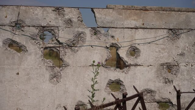 Wall with holes from shelling. Concrete wall with numerous holes and cracks, witness of military operations. Concept of war, destruction, memories