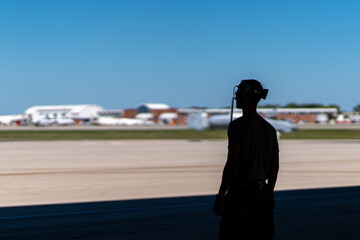A man wearing a headset stands on the runway, looking out over the tarmac